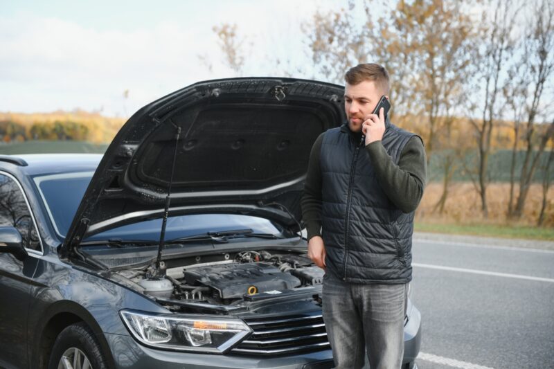 momak stoji pored pokvarenog automobila i priča preko telefona