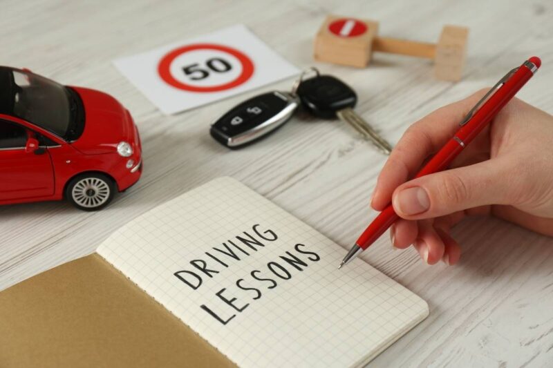 prikaz sveske na kojoj piše auto škola, ključevi od automobila, automobil i znak 50 za brzinu