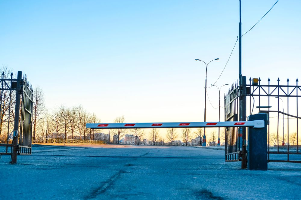 Automatska parking rampa sa crveno-belim oznakama postavljena između metalnih ograda na ulazu u ograđeni parking prostor