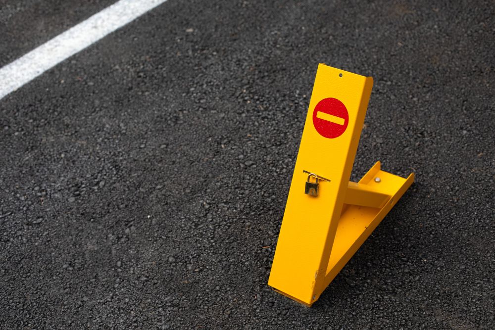 Žuta metalna parking barijera sa lokotom i znakom zabrane ulaska, postavljena na asfaltu radi zaštite rezervisanog parking mesta