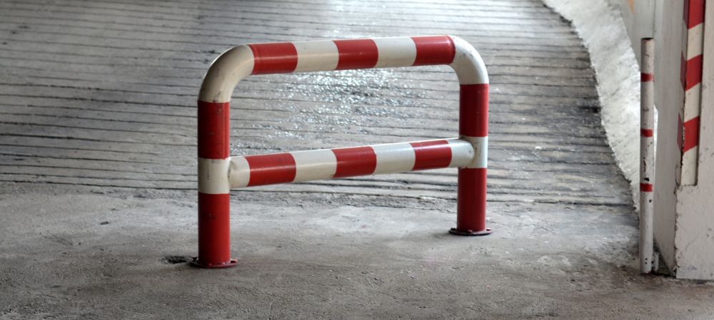 Crveno-bela metalna zaštitna barijera pričvršćena za betonsku podlogu na prilazu stambenoj zgradi.